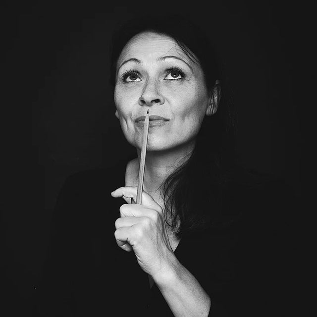 Black and white portrait of a woman holding a pencil near her face against a dark background